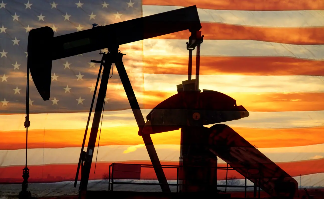 Oil pump jack silhouetted against an American flag at sunset